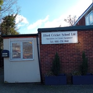 Exterior entrance to the Ilford Cricket School — a white-rendered extension with heavily grilled window on a single-storey red brick building, with a taller building behind that.